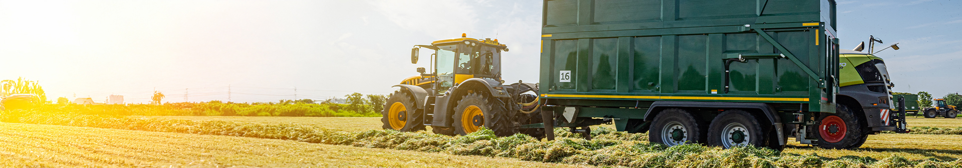 Tractor equipped with agricultural tyres towing a trailer during field harvesting on a sunny day.