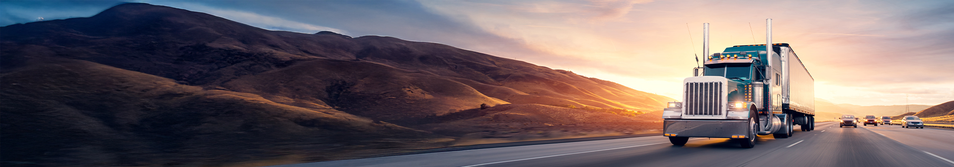 Semi-truck equipped with all-position truck tires driving on a highway through mountainous terrain at sunset.