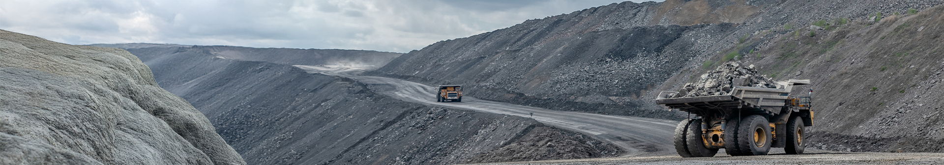 Dump trucks fitted with giant tires hauling heavy loads of rocks on a rugged mining road with steep slopes.