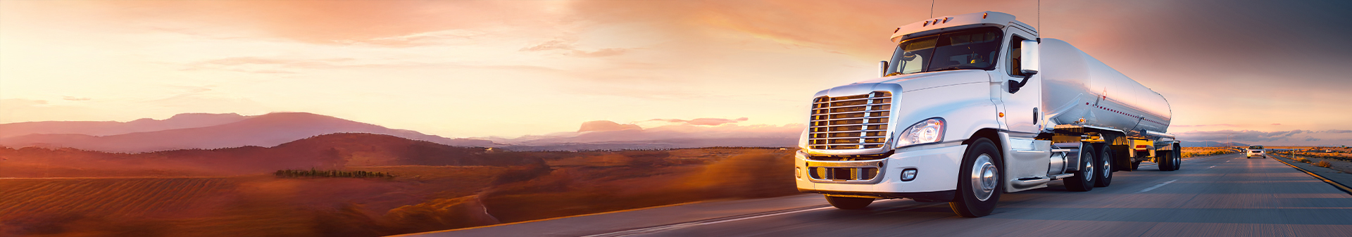 Long-haul truck equipped with durable tires towing a tanker trailer on a highway at sunset.