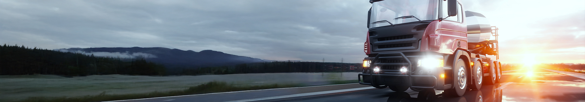 Truck equipped with regional tires transporting cargo along a scenic highway at sunrise.