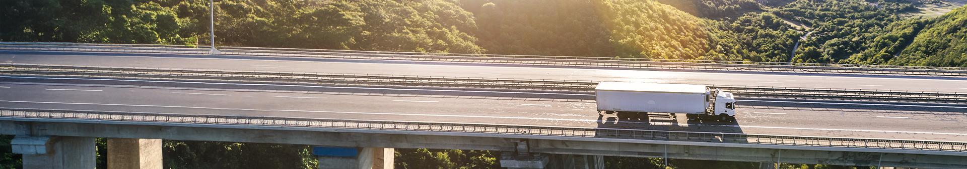 Truck with reliable steer tires traveling on a highway bridge surrounded by lush greenery.