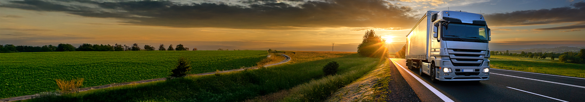 Truck with trailer tires driving along a scenic rural highway at sunset.