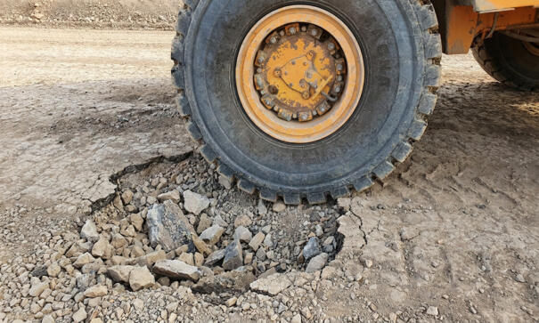 Close-up van een band van een starre dumper bij een beschadigde transportweg met kuilen en losse stenen